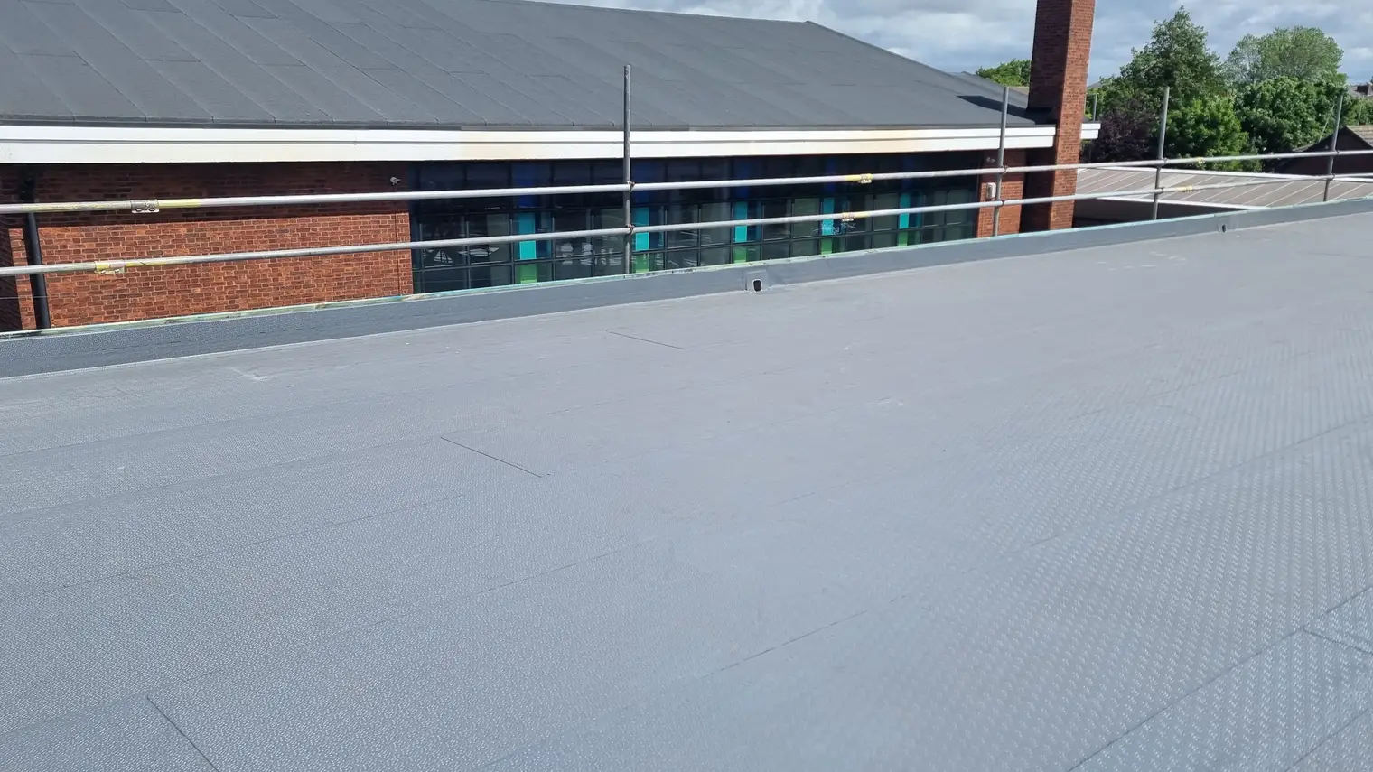 Finished grey single ply roof beside a brick building with large windows